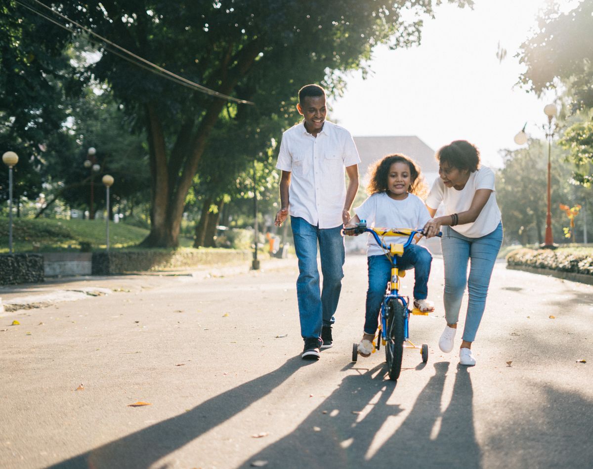 Adults helping a child ride a bicycle