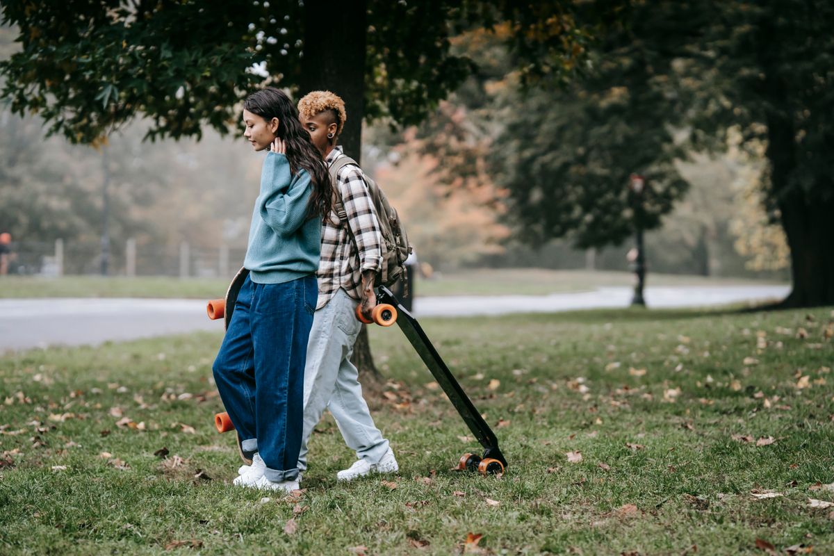 Two friends carrying skateboards through a park